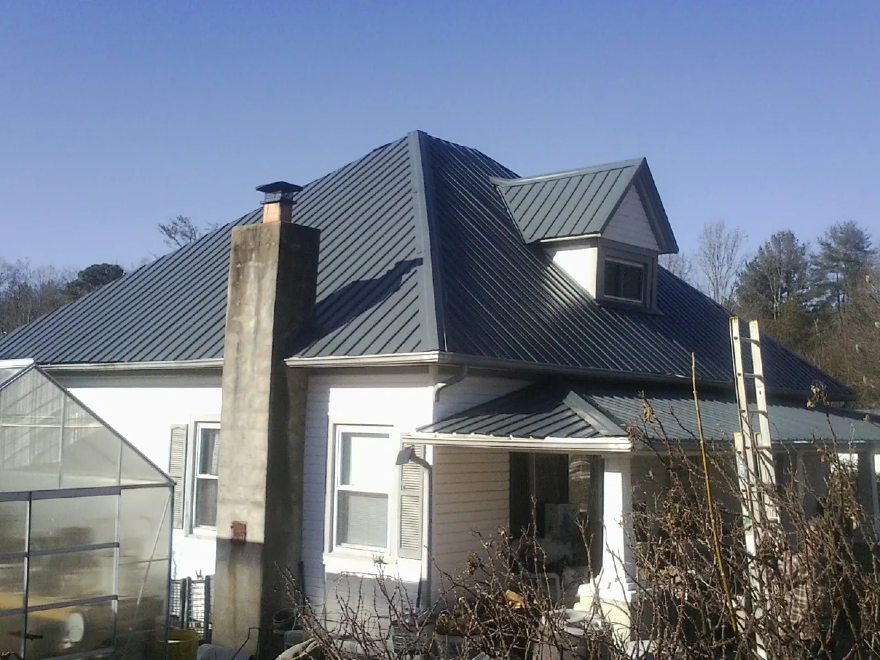Dark blue standing seam metal roof on a white farmhouse with dormer — Slate & Tile Roof Repair by Roofing Brothers in Little Elm