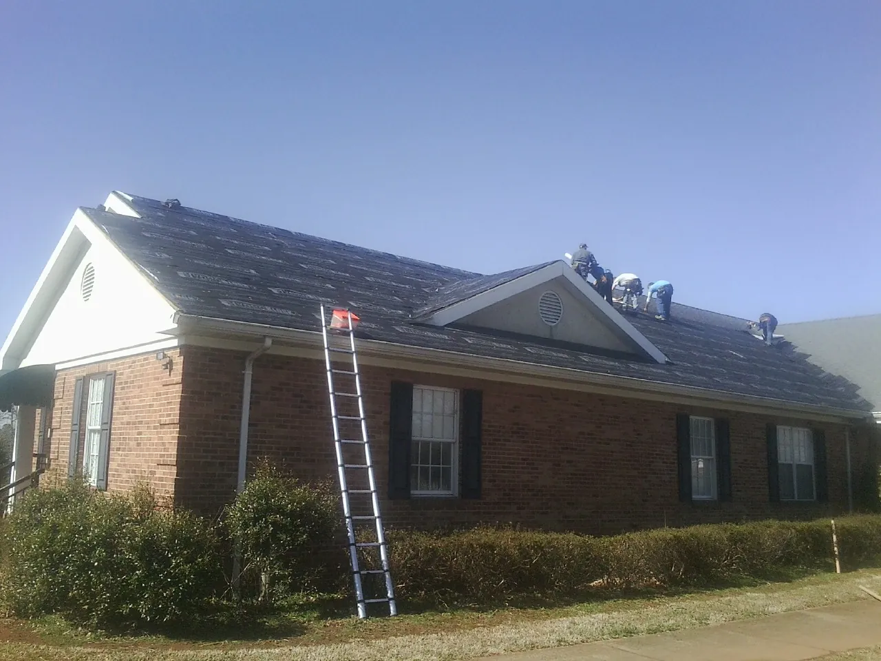Crew tearing shingles off a brick ranch roof with a ladder set — Metal Roof Repair work by our crew in Little Elm