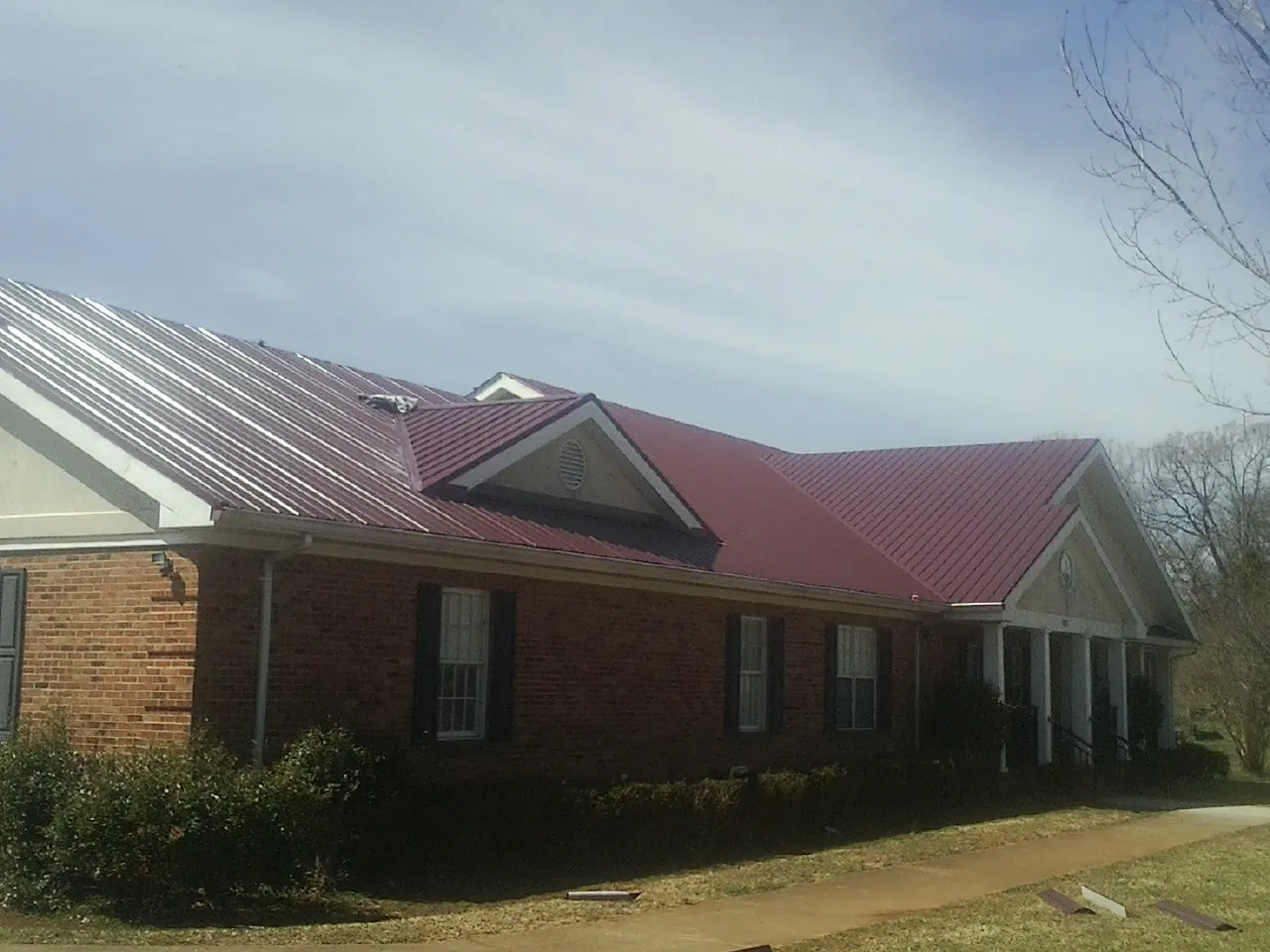 Red metal roof with gabled entries on a long brick building, from a Hail Damage Roof Repair job in Little Elm