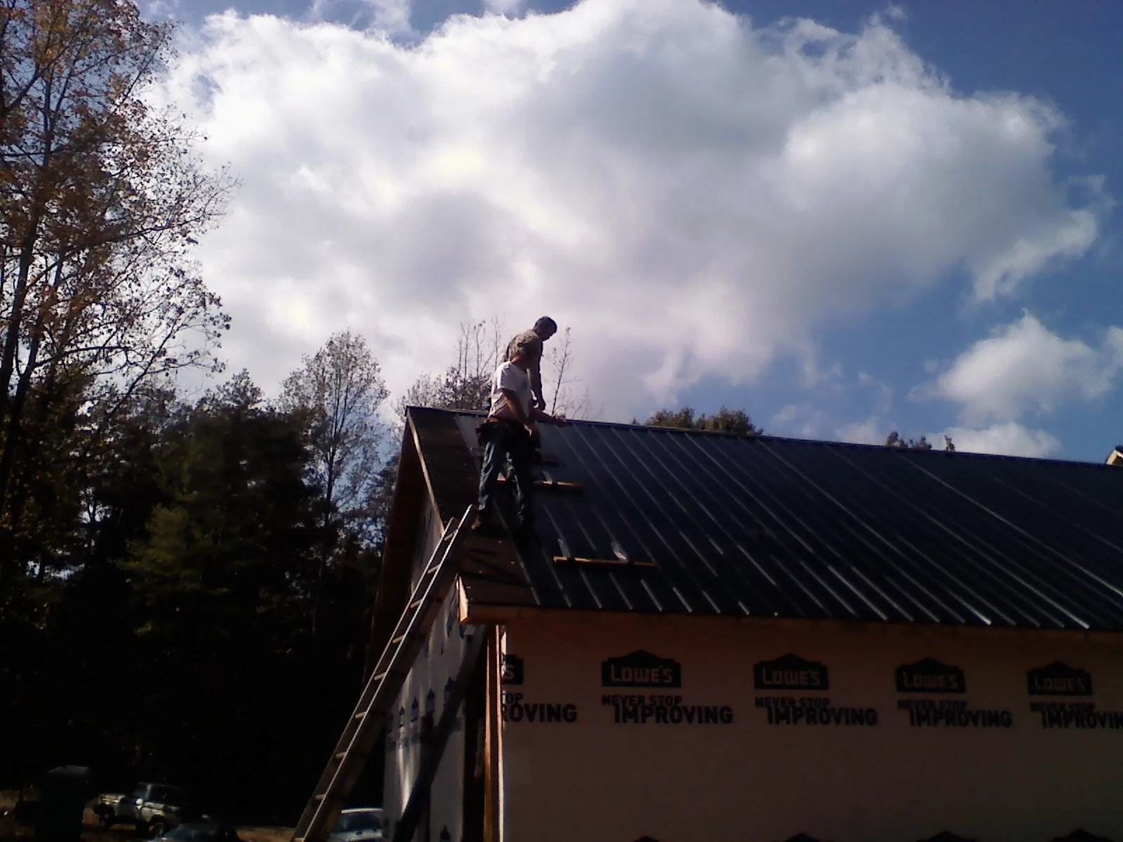Roofer fastening dark metal panels high against a cloudy sky, from a Roof Inspection job in Little Elm