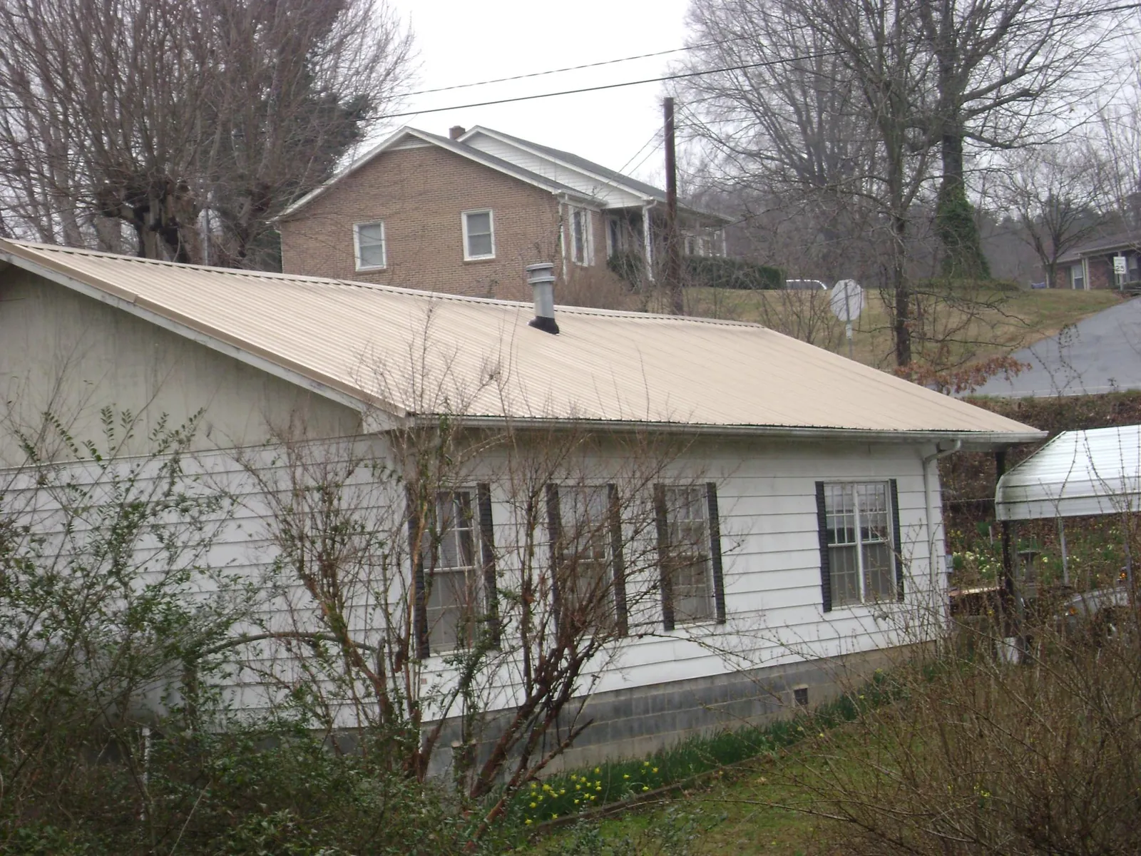 Tan metal roof on a white sided house set into a hillside — Commercial Roofing by Roofing Brothers in Little Elm
